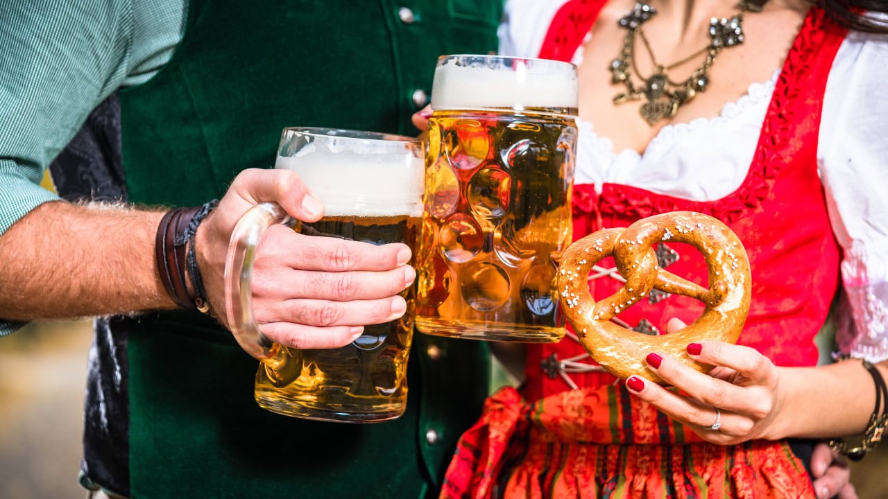 Residents attending New Jersey Oktoberfest event wearing traditional Bavarian outfit enjoying beers and a pretzel. Image produced by More Jersey.