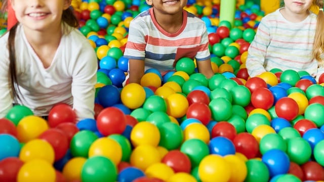 Three kids playing in colorful ball pit at New Jersey play center.
