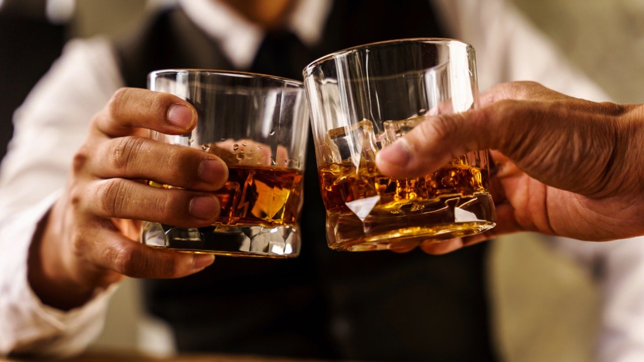 Two friends clinking glasses during cheers at a whiskey event in New Jersey.