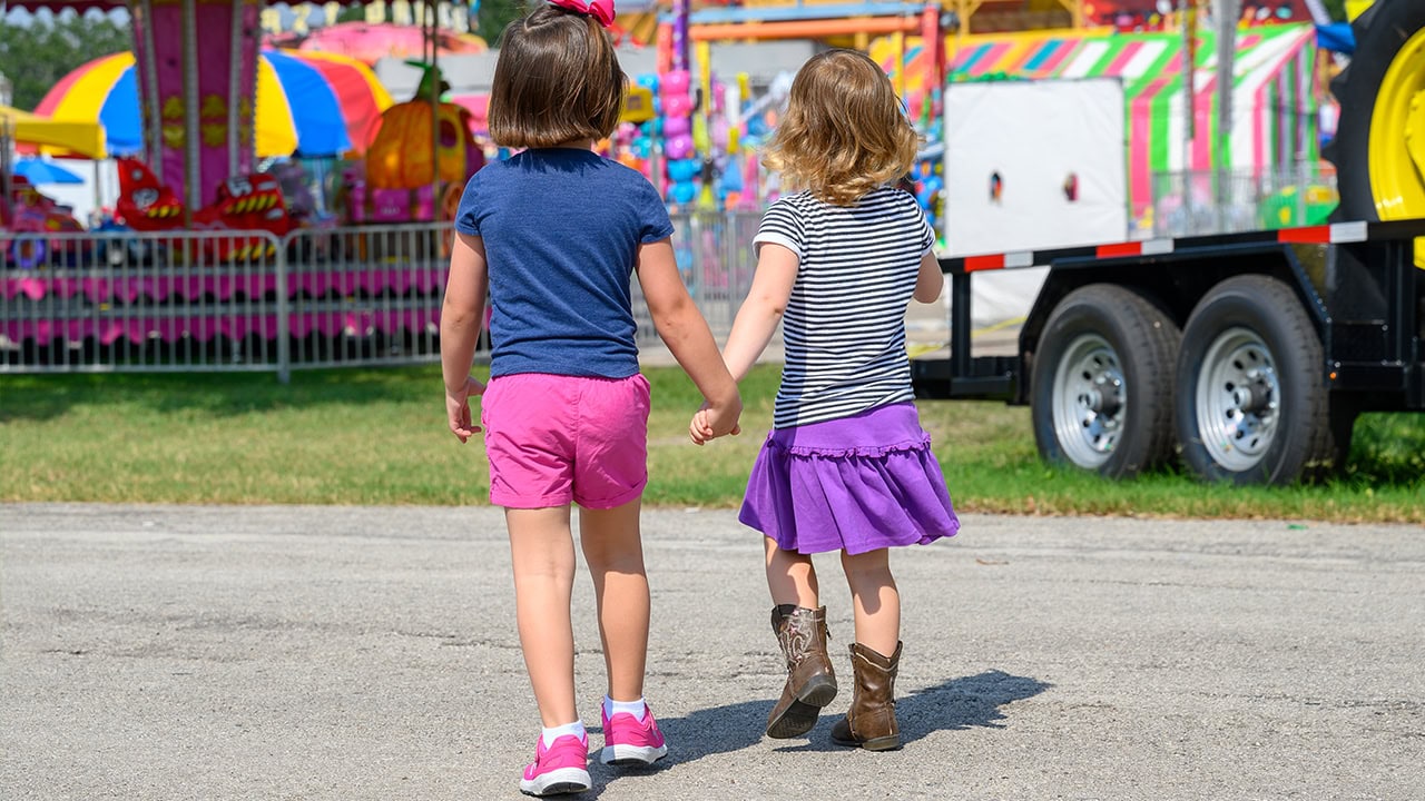 Two young girls holding hands walking into New Jersey county fair. Image produced by More Jersey.