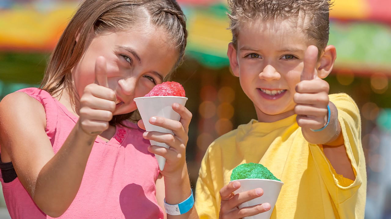 Two young kids holding snow cones with their thumbs up at New Jersey state fair. Image produced by More Jersey.