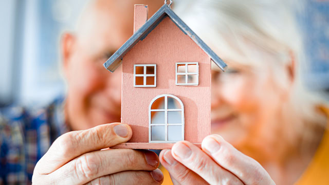  White senior couple holding a small home model.