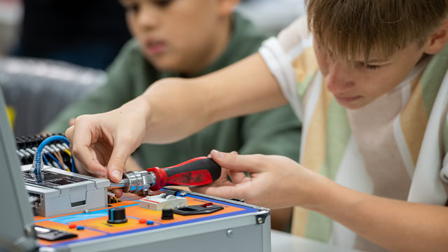 White STEM student using a screwdriver while working on robot machinery.