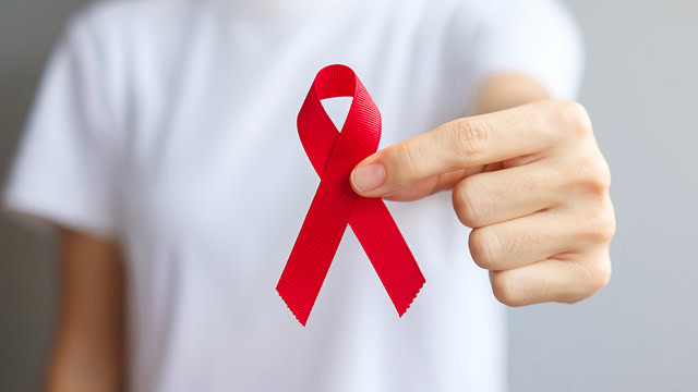 White woman holding a red ribbon for AIDS awareness.