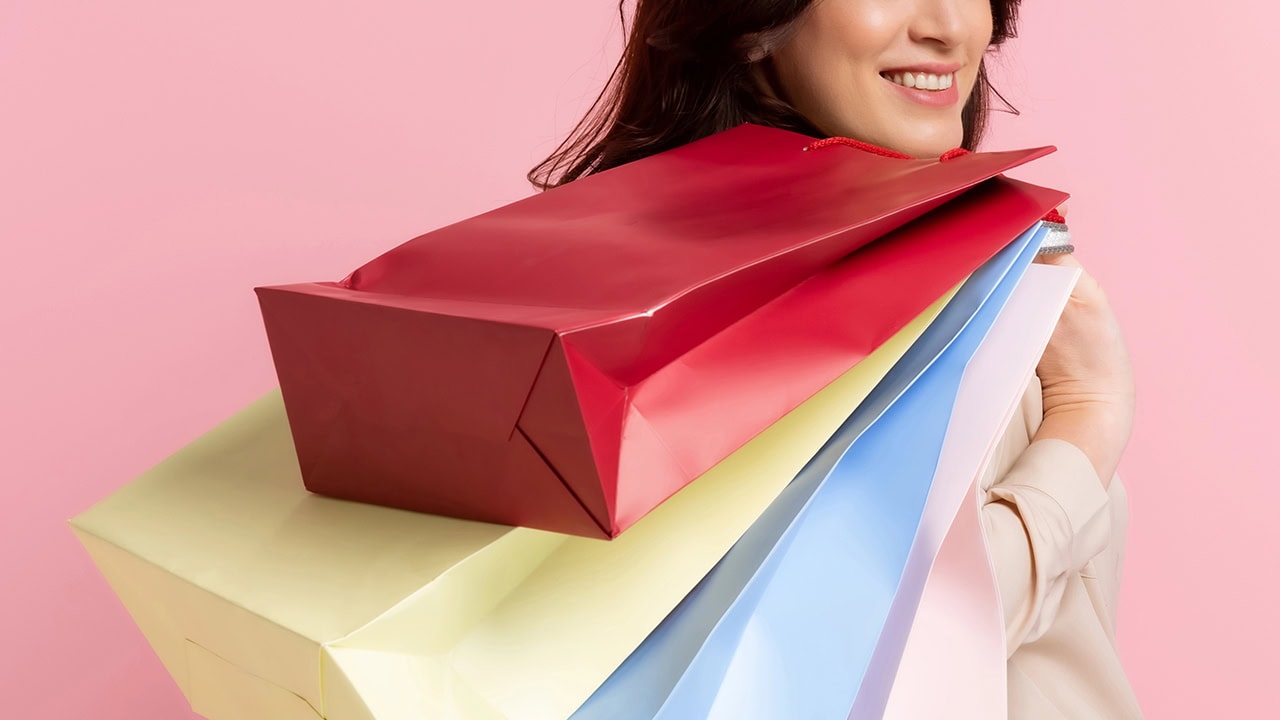 Woman holding colorful shopping bags on pink background. Image produced by More Jersey.