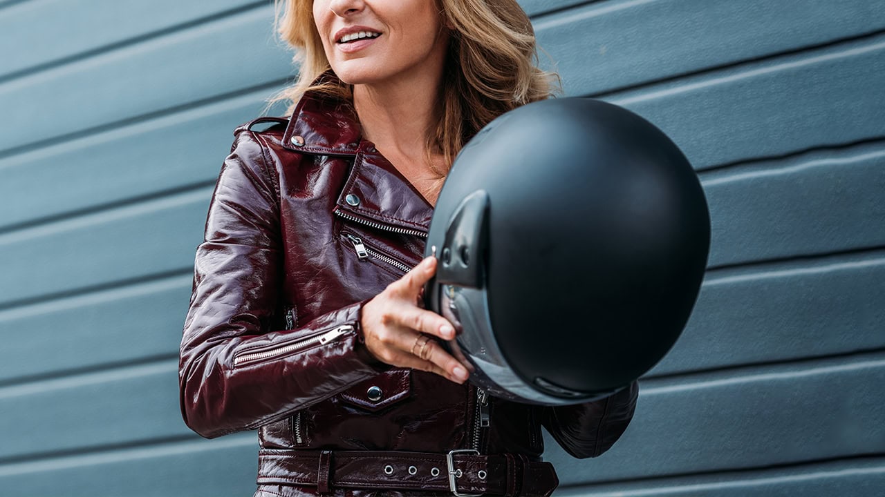 Woman in leather jacket holding motorcycle helmet.