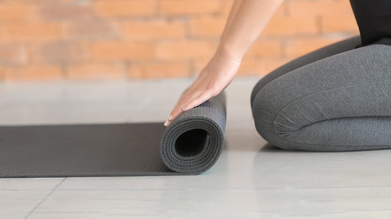 Woman unrolling yoga mat with brill wall in the background.