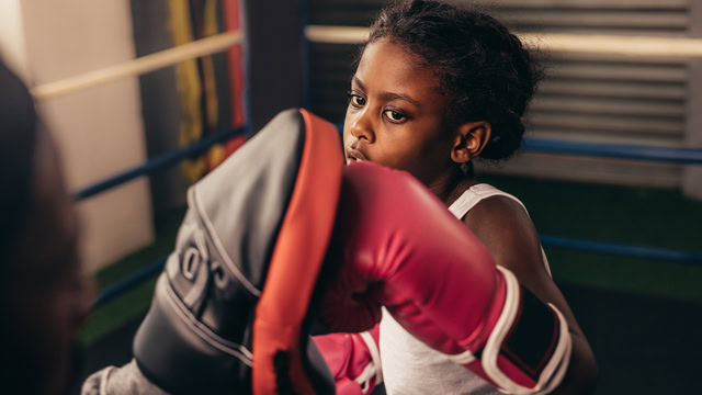 Young African American girl practicing punches on a punching pad at a local boxing gym.