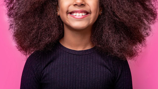 Young biracial girl smiling in front of a pink color background.