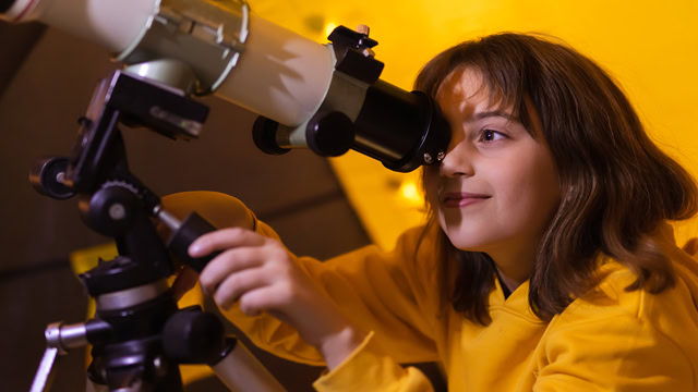 Young girl using a telescope from inside a tent.