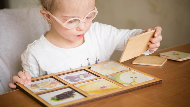 Young girl with Down syndrome playing with a wooden matching game set.