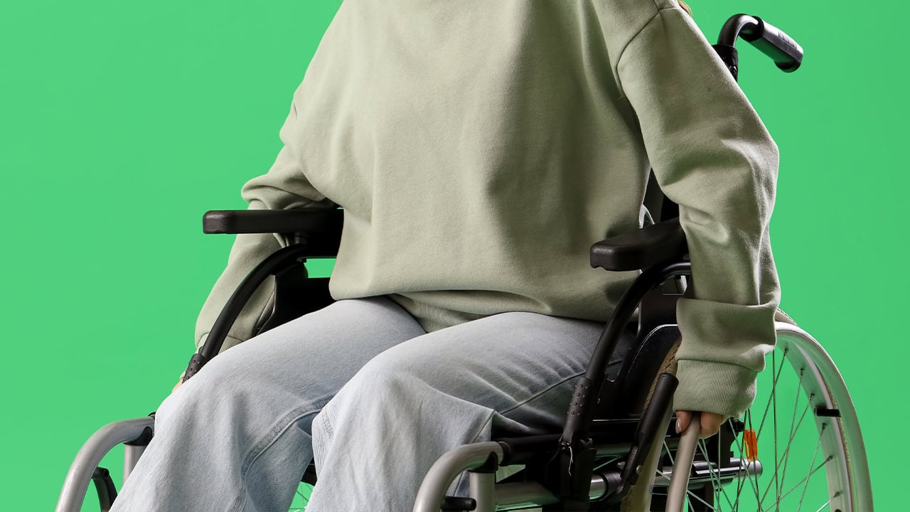 Young redhead woman in a wheelchair in front of a green color background. Image produced by More Jersey.