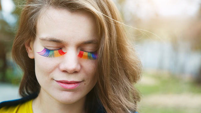  Young white woman smiling with rainbow LGBTQ+ eyelashes.